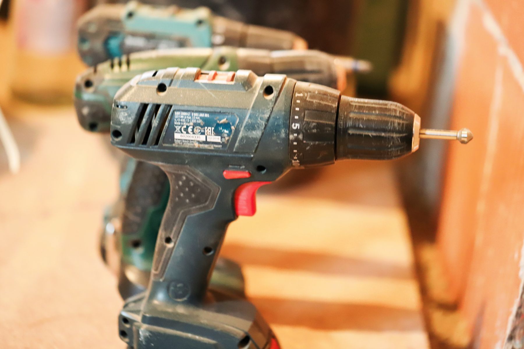 A row of cordless drill drivers resting on a wooden workbench